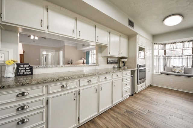 kitchen featuring visible vents, white cabinets, light wood-style floors, stainless steel oven, and tasteful backsplash