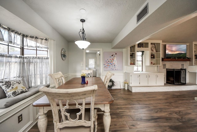 dining area with dark wood-style floors, visible vents, a fireplace with raised hearth, wainscoting, and a decorative wall