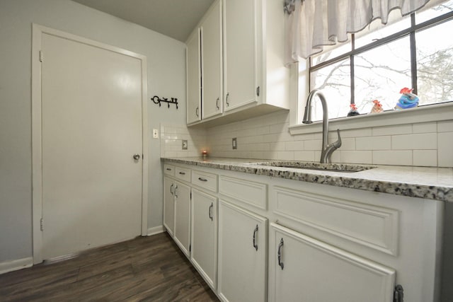 kitchen featuring a sink, light stone counters, white cabinets, decorative backsplash, and dark wood-style flooring