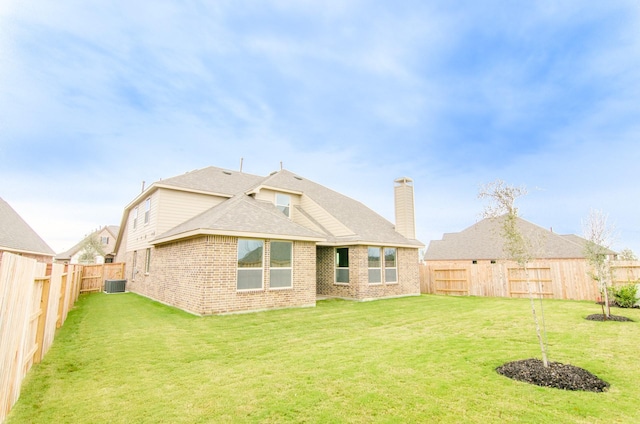 rear view of house featuring central air condition unit, a chimney, brick siding, a fenced backyard, and a yard