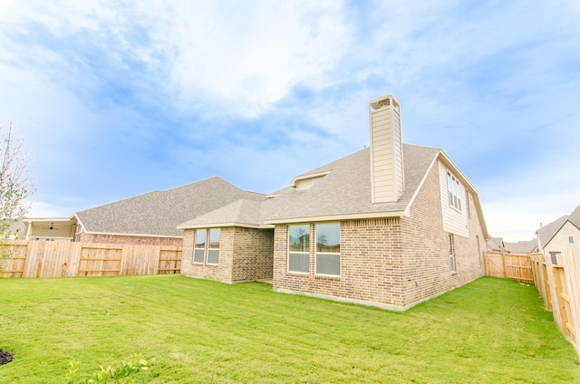 back of property featuring a fenced backyard, a chimney, brick siding, and a yard