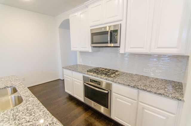 kitchen featuring white cabinetry, stainless steel appliances, decorative backsplash, dark wood finished floors, and arched walkways
