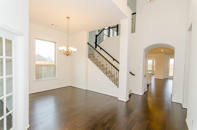 interior space with baseboards, stairs, dark wood-type flooring, arched walkways, and an inviting chandelier