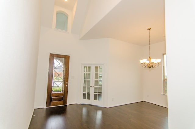 foyer entrance with french doors, wood finished floors, baseboards, a towering ceiling, and an inviting chandelier