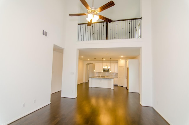 unfurnished living room featuring dark wood-style floors, baseboards, visible vents, arched walkways, and ceiling fan