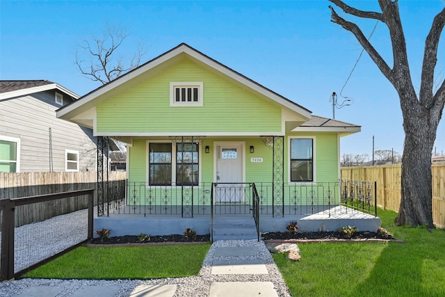 bungalow-style home with covered porch, fence, and a front lawn