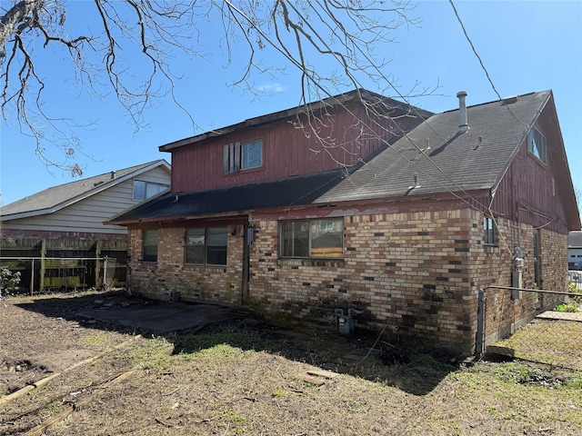 rear view of property featuring a shingled roof, fence, a patio, and brick siding