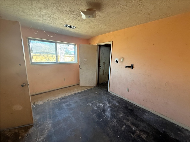 spare room featuring a textured ceiling, visible vents, and concrete flooring