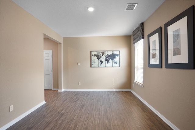 empty room featuring dark wood-style floors, baseboards, and visible vents