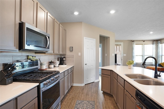 kitchen with stainless steel appliances, tasteful backsplash, light countertops, a sink, and wood finished floors