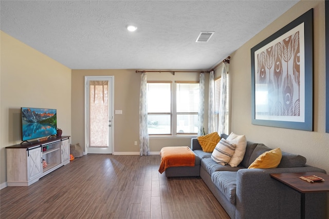 living area with a textured ceiling, wood finished floors, visible vents, and baseboards