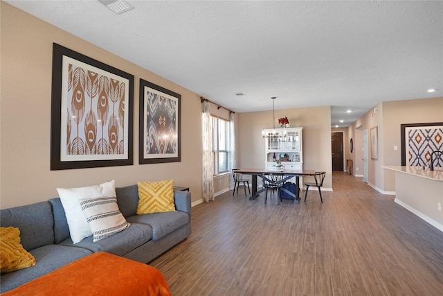 living area featuring visible vents, a textured ceiling, baseboards, and wood finished floors