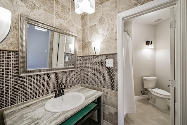 bathroom featuring vanity, baseboards, visible vents, tile walls, and toilet