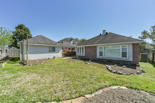 back of property with a fenced backyard, a yard, roof with shingles, brick siding, and a chimney