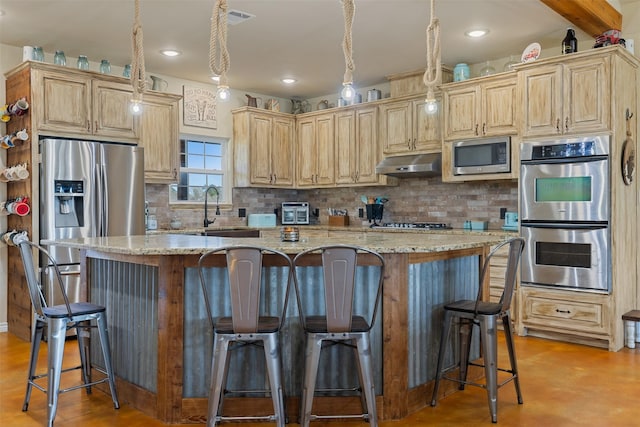 kitchen featuring under cabinet range hood, a kitchen island, a sink, appliances with stainless steel finishes, and decorative backsplash