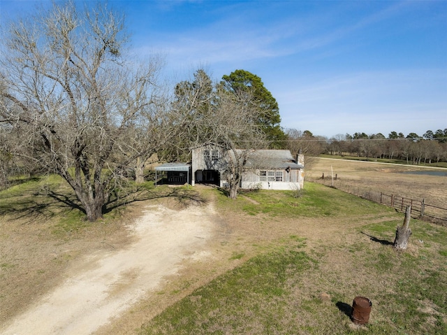 view of front of house with a front yard, a rural view, driveway, and fence