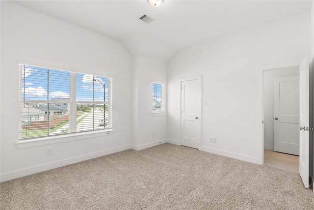 empty room featuring baseboards, visible vents, vaulted ceiling, and light colored carpet