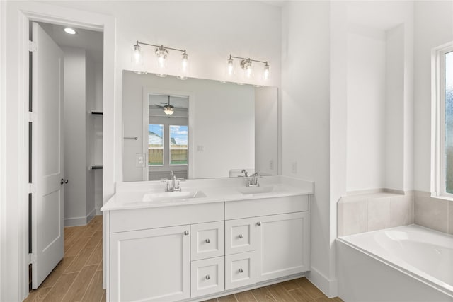 bathroom featuring double vanity, wood tiled floor, a sink, and a bath