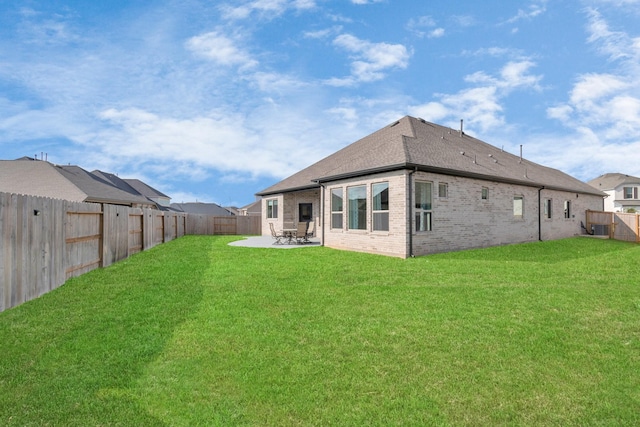 rear view of property featuring a lawn, brick siding, a patio, and a fenced backyard