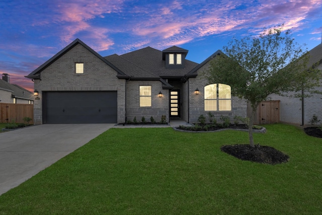 french provincial home featuring brick siding, roof with shingles, concrete driveway, fence, and a front lawn