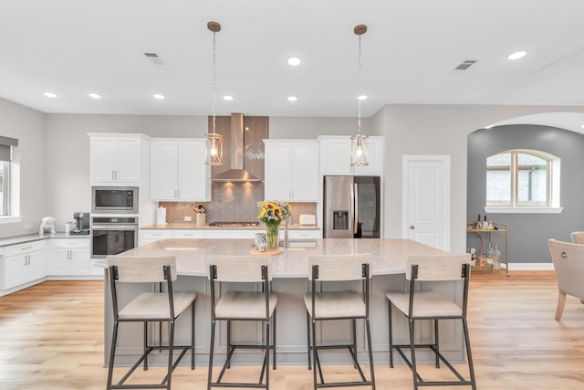 kitchen featuring white cabinets, stainless steel appliances, visible vents, wall chimney exhaust hood, and decorative backsplash