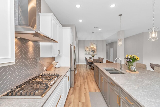 kitchen with a sink, wall chimney exhaust hood, light wood-style flooring, appliances with stainless steel finishes, and white cabinetry