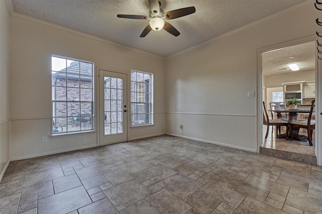 empty room with a wealth of natural light, wainscoting, and a textured ceiling