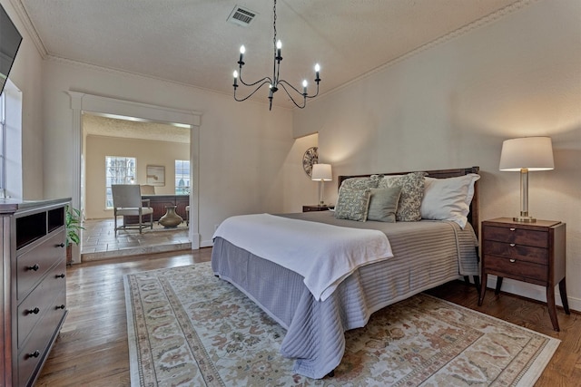 bedroom featuring a textured ceiling, a chandelier, wood finished floors, visible vents, and crown molding