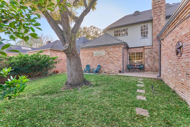 back of house featuring a patio area, a lawn, and brick siding