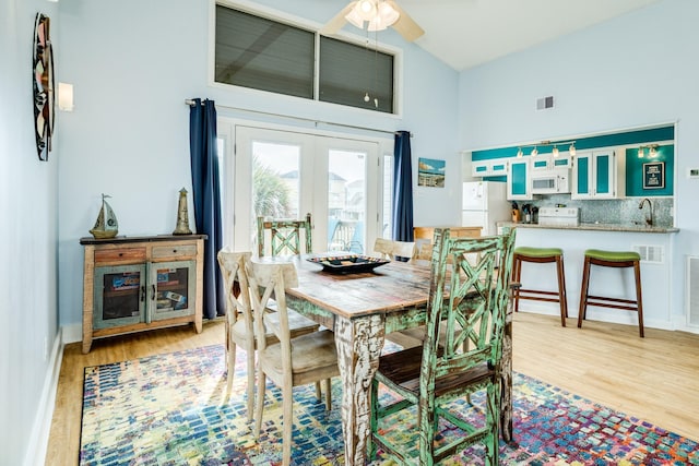 dining room with french doors, visible vents, light wood-style floors, high vaulted ceiling, and baseboards