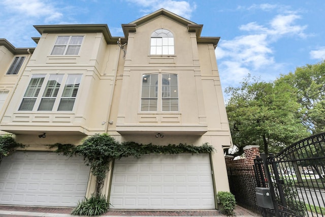 view of side of property with decorative driveway, fence, an attached garage, and stucco siding