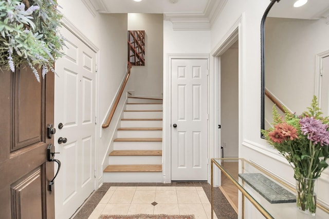 foyer featuring light tile patterned floors, stairs, baseboards, and crown molding