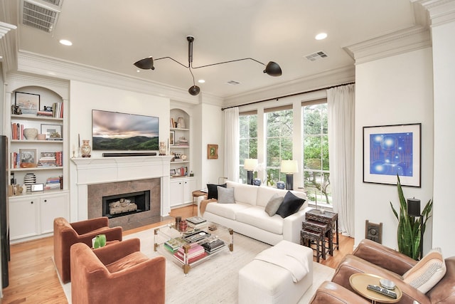 living area with visible vents, built in features, ornamental molding, light wood-type flooring, and a high end fireplace