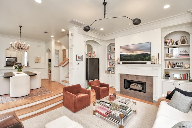 living room featuring a fireplace, built in features, stairs, light wood-style floors, and ornamental molding