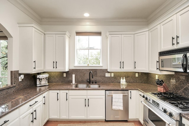 kitchen featuring arched walkways, stainless steel appliances, white cabinetry, a sink, and plenty of natural light