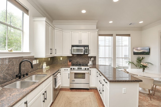 kitchen featuring crown molding, stainless steel appliances, white cabinets, a sink, and a peninsula