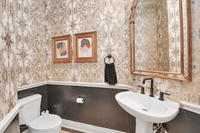 half bathroom with a sink, toilet, and wallpapered walls