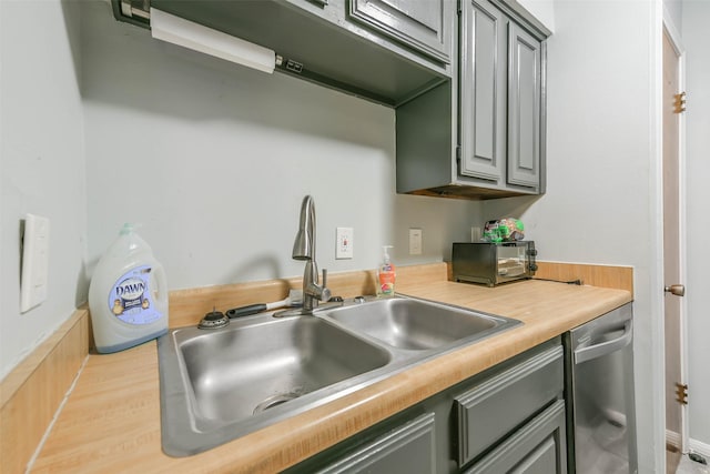 kitchen featuring stainless steel dishwasher, gray cabinets, and a sink