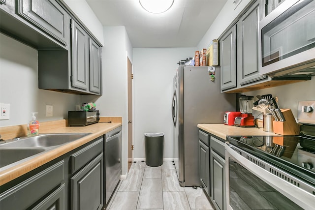 kitchen featuring light countertops, appliances with stainless steel finishes, a sink, and gray cabinetry