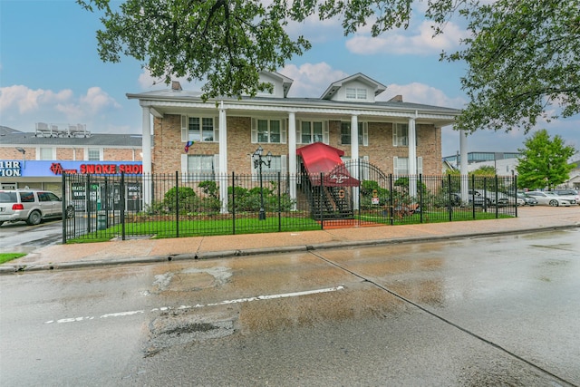 greek revival house featuring a fenced front yard, brick siding, and uncovered parking