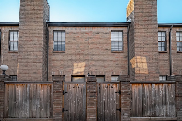 rear view of property with brick siding, fence, and a gate