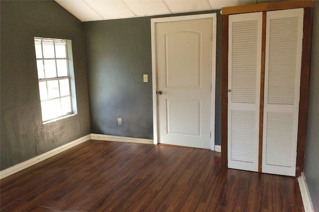 unfurnished bedroom with vaulted ceiling, dark wood-style flooring, a closet, and baseboards