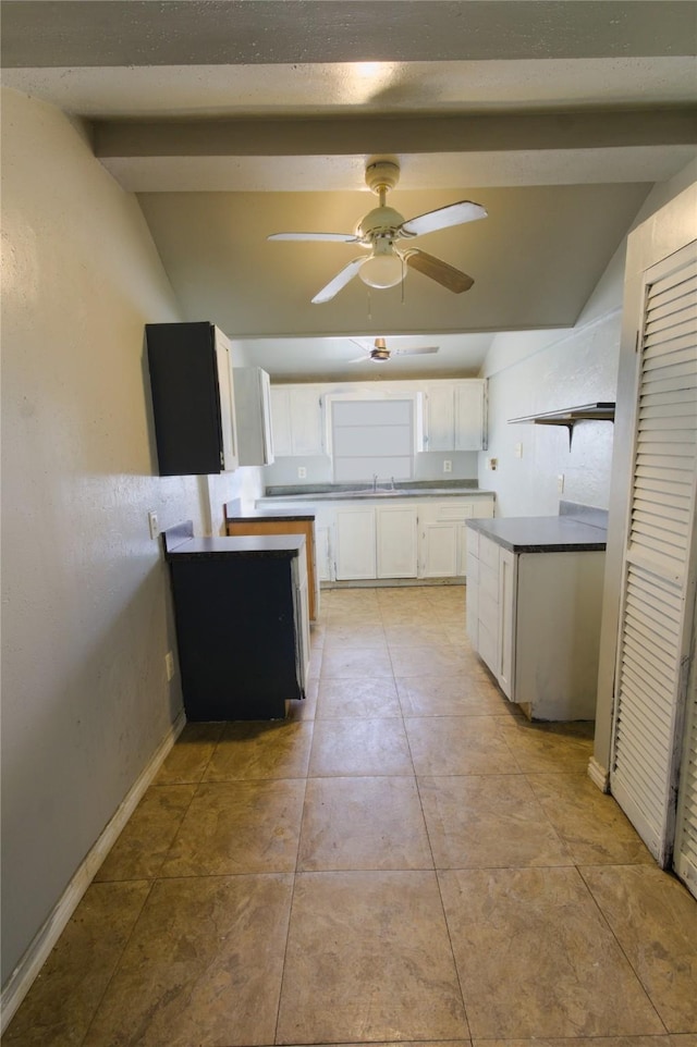 kitchen featuring vaulted ceiling with beams, dark countertops, white cabinetry, a sink, and ceiling fan