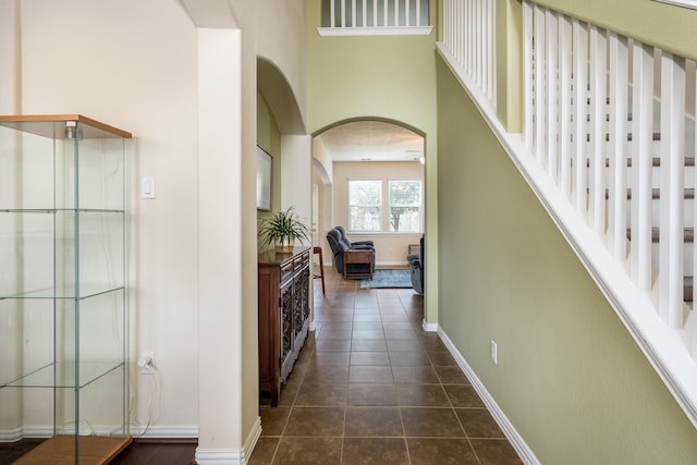 hallway featuring arched walkways, baseboards, and dark tile patterned flooring