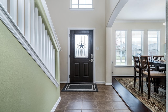 foyer with a wealth of natural light, arched walkways, dark tile patterned flooring, and ornamental molding