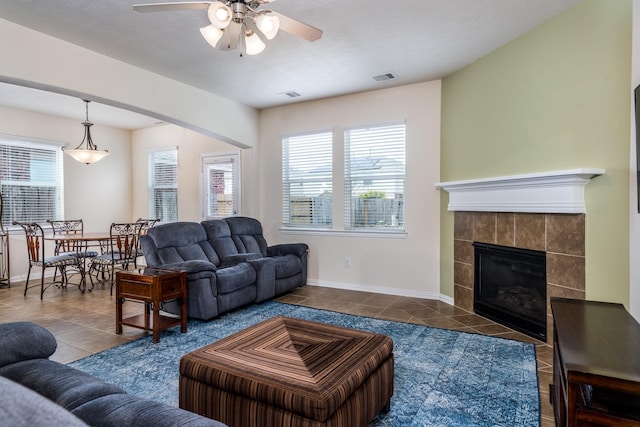 tiled living room featuring visible vents, baseboards, ceiling fan, and a tiled fireplace