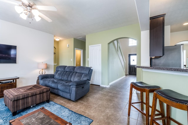 tiled living area featuring a ceiling fan, baseboards, and arched walkways