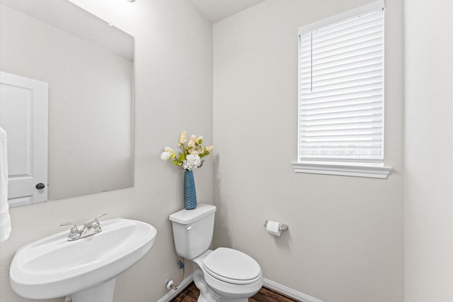 half bathroom with toilet, baseboards, a sink, and wood finished floors