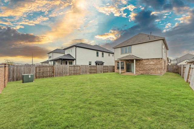 rear view of house featuring a yard, brick siding, and a fenced backyard