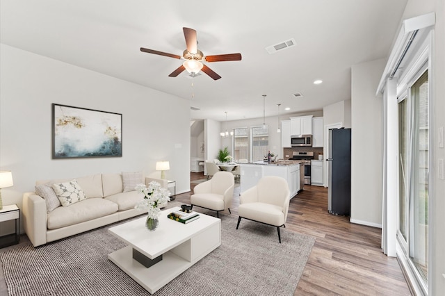 living room with light wood finished floors, recessed lighting, visible vents, baseboards, and ceiling fan with notable chandelier